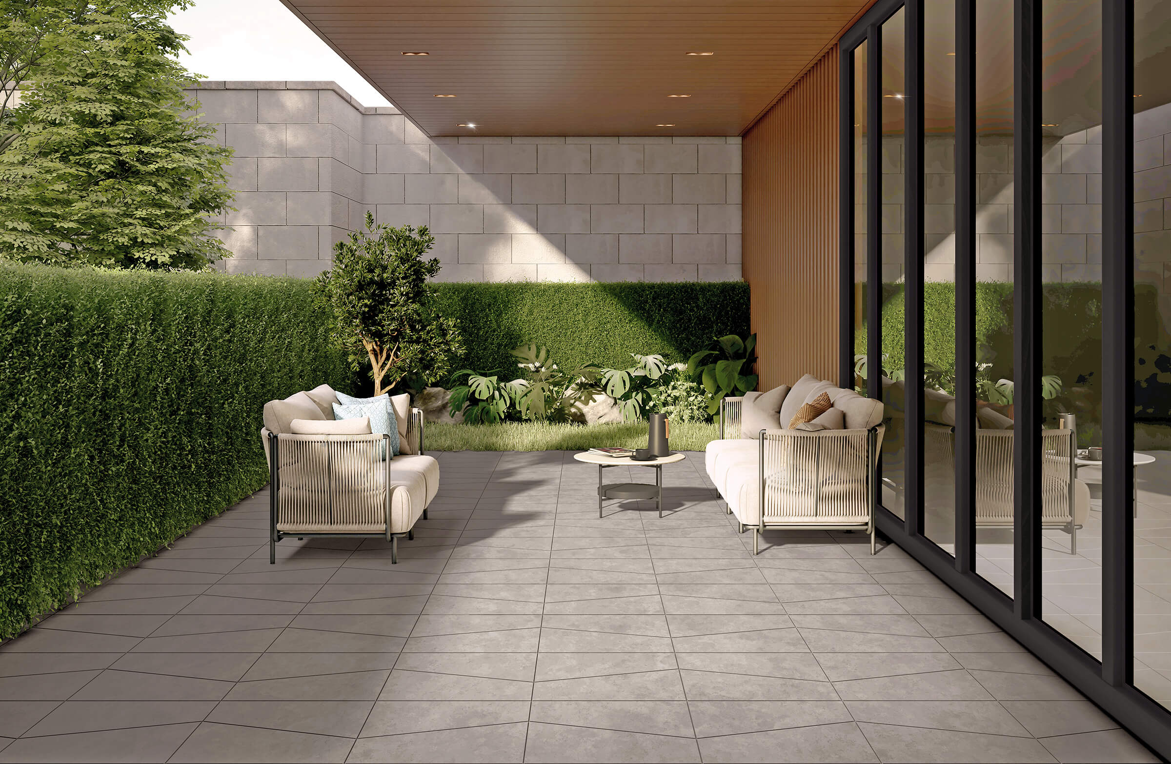 Modern patio with beige sofas, lush greenery, and a smooth paved floor. Reflective glass panels enhance the spacious and serene outdoor ambiance.