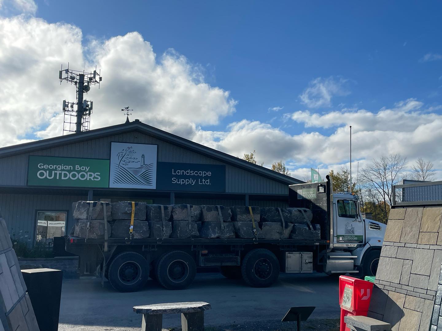 A truck is parked outside Georgian Bay Outdoors, Landscape Supply Ltd., beneath a cloudy sky, with signs and stone materials visible.