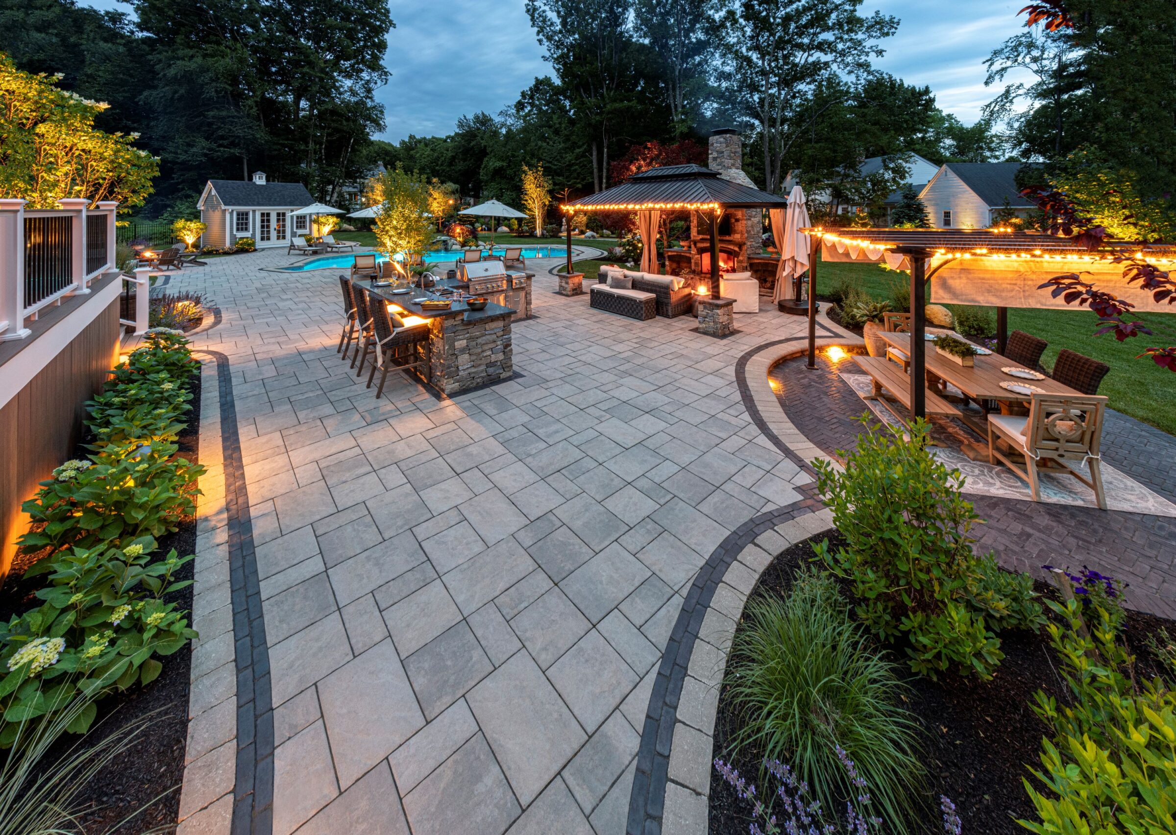 Beautiful backyard patio with seating areas, ambient lighting, fire pit, greenery, and a swimming pool, creating an inviting and serene outdoor space.
