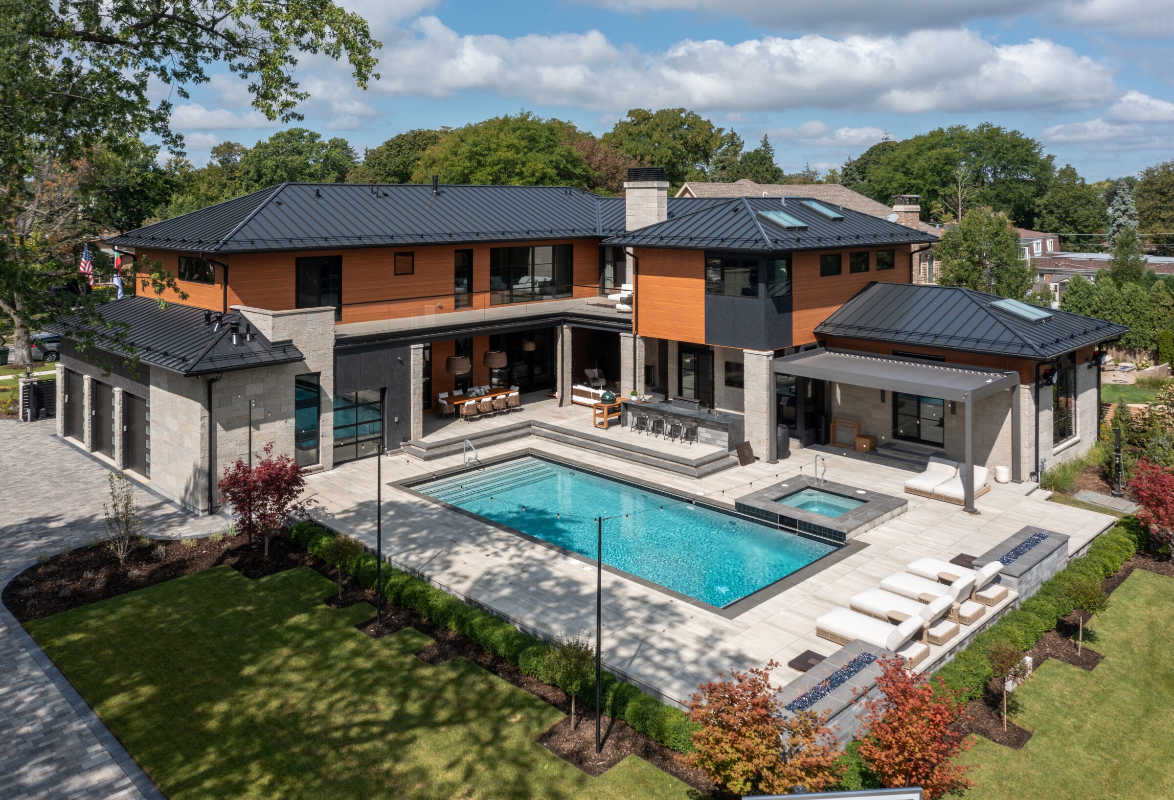 Modern two-story house with a sleek design, spacious patio, swimming pool, and surrounding greenery under a partly cloudy sky.