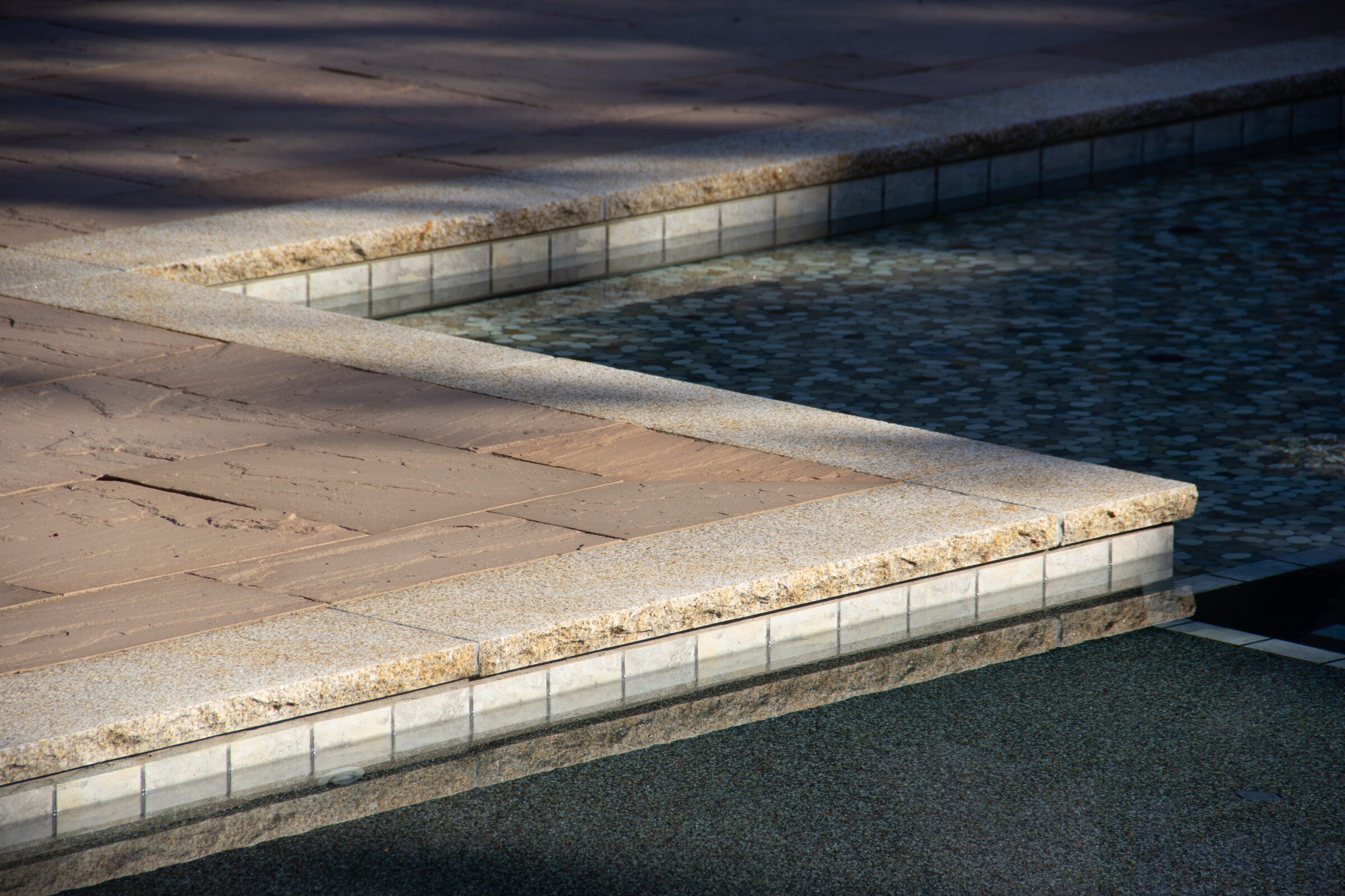 Geometric stone path and shallow reflecting pool, casting shadows on a sunny day. Peaceful, minimalistic outdoor design.