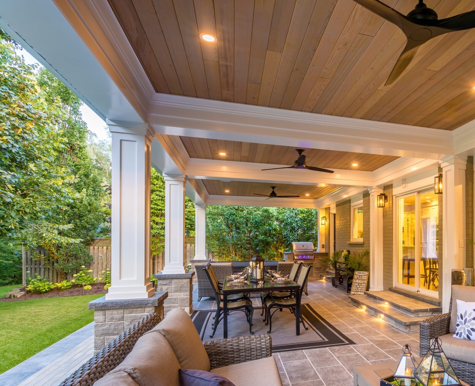 Elegant, covered patio featuring comfortable seating, dining area, decorative lighting, and lush garden view, creating a cozy outdoor living space.