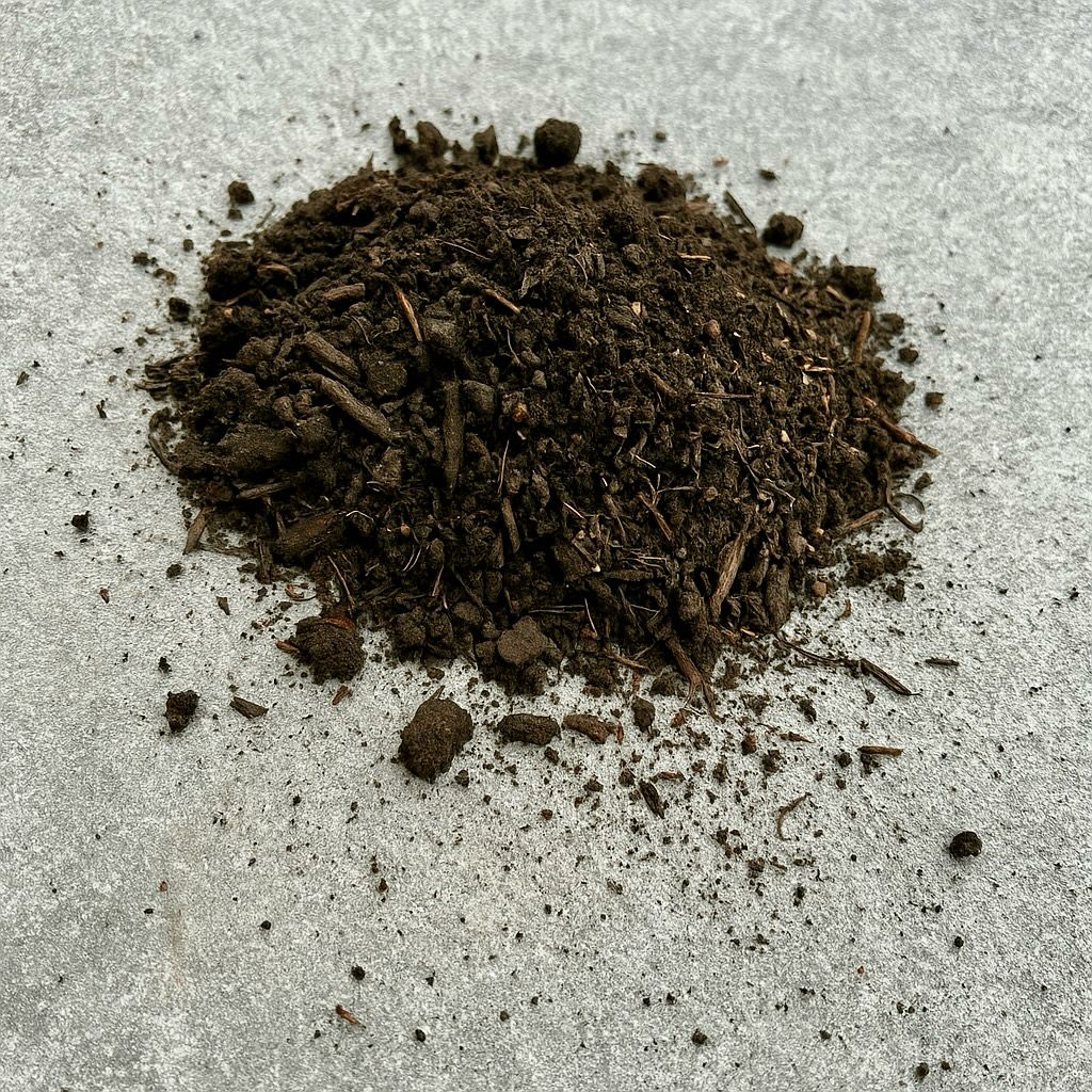 A small pile of dark soil rests on a smooth, light gray surface, with scattered debris surrounding it.