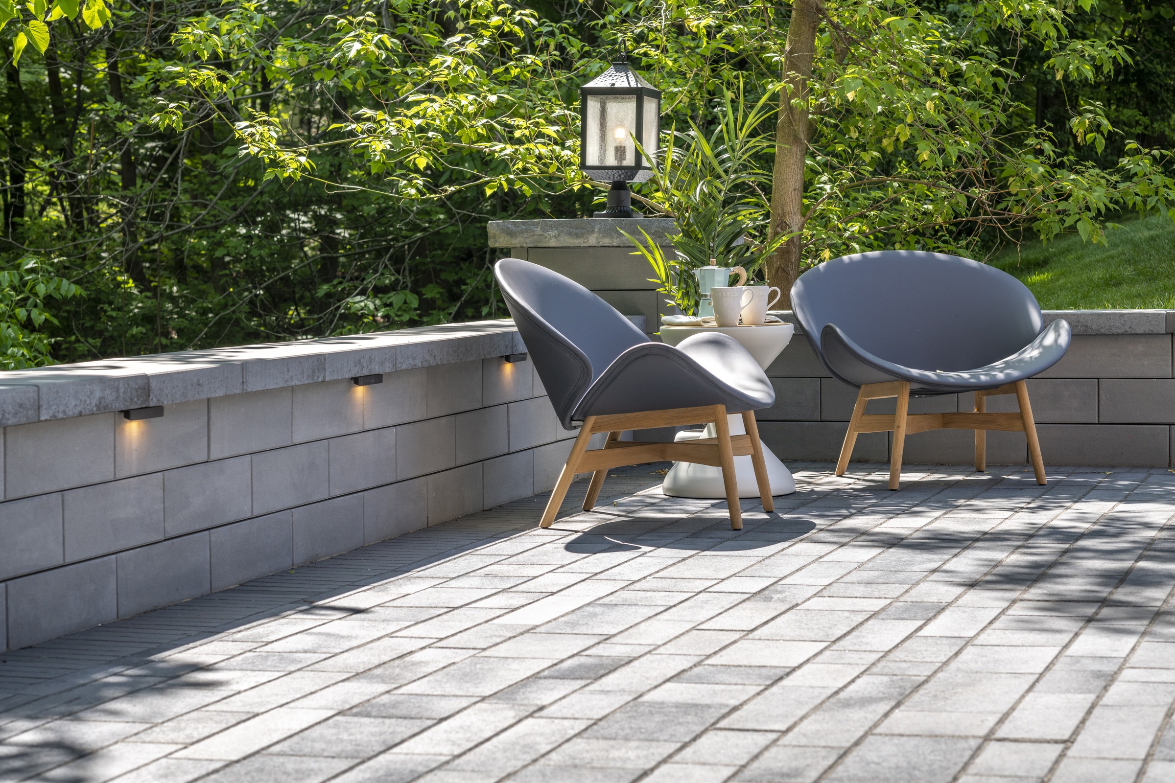 Modern patio with two stylish chairs, a small table, and a lantern amid lush greenery, creating a serene outdoor seating area.
