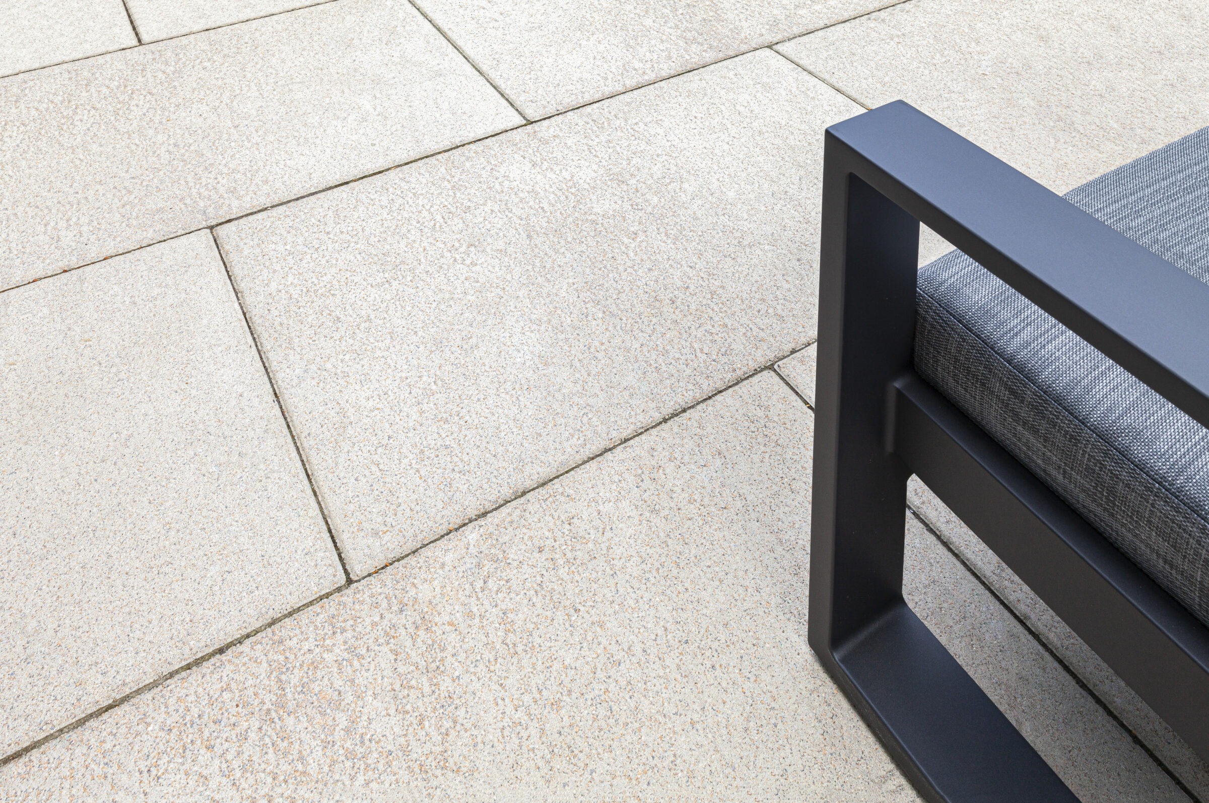 Close-up of a modern outdoor chair on light stone tiles. Minimalist design with metal frame and gray cushioned seat.