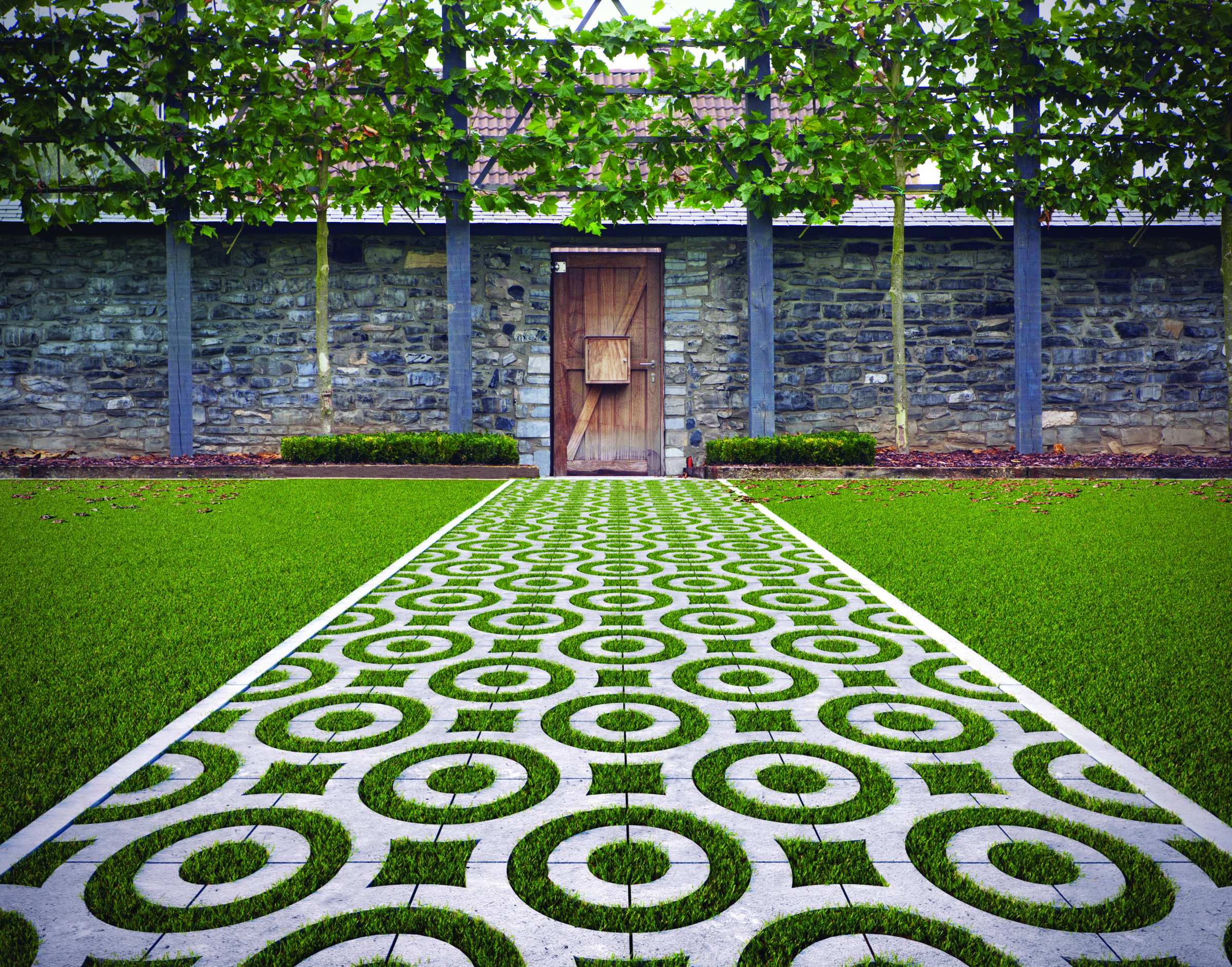 Patterned path leads to a wooden door on a stone wall, surrounded by green grass and trees, with no landmarks or people present.