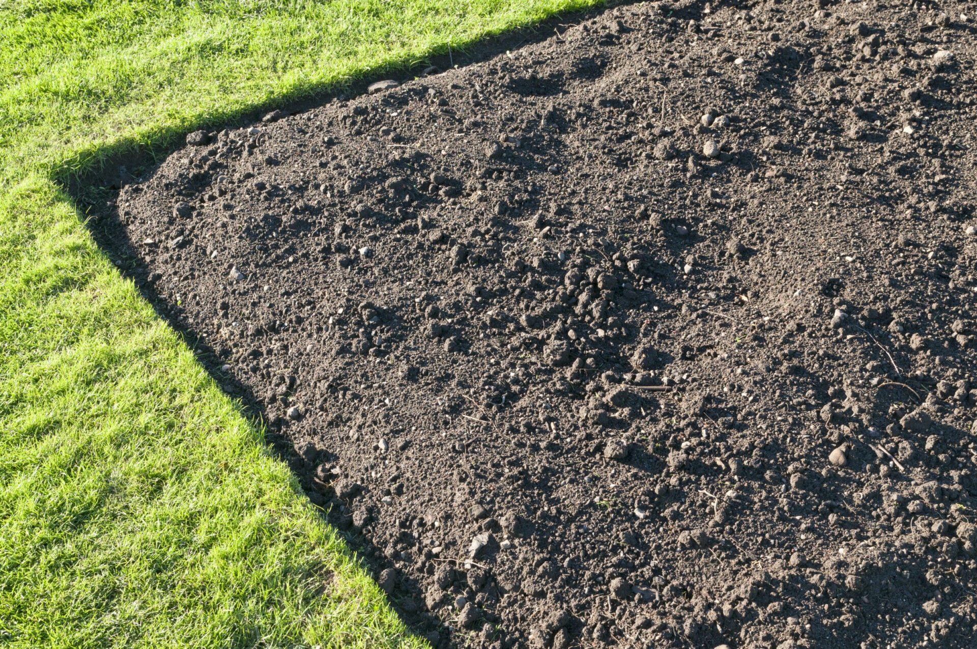 Freshly tilled soil beside vibrant green grass, forming a clear boundary. The well-maintained garden area suggests preparation for planting.