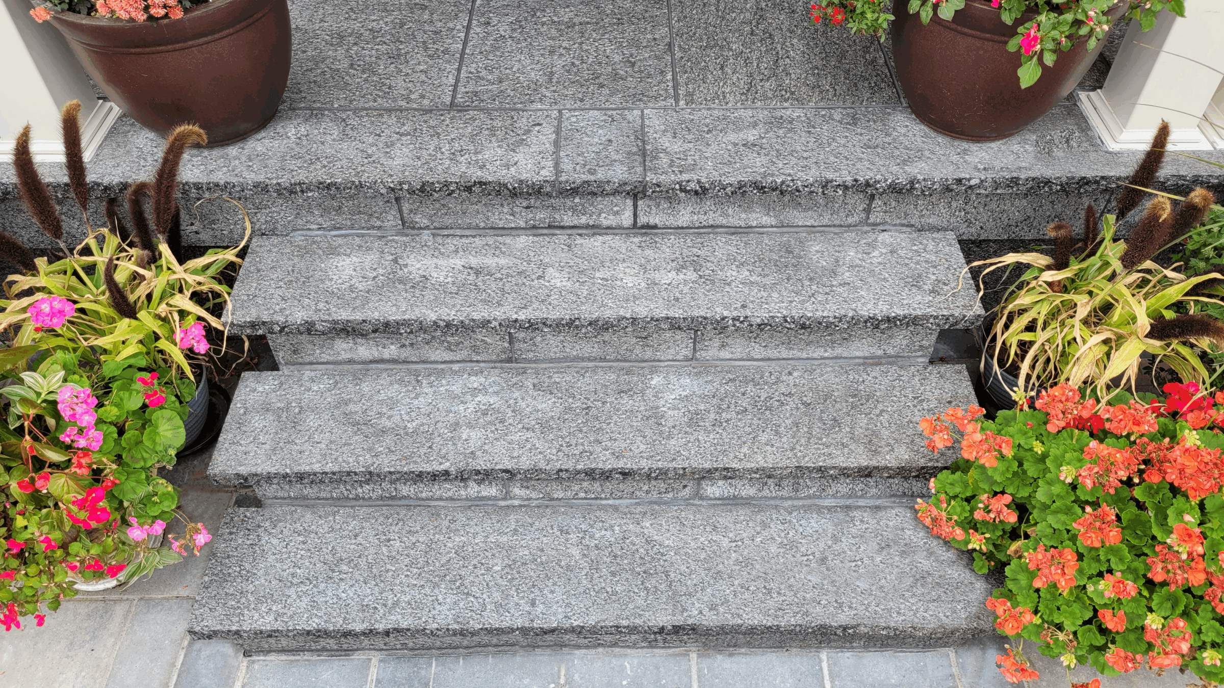 Gray stone steps with vibrant flower pots on both sides, displaying pink and orange blossoms, create a welcoming entrance.