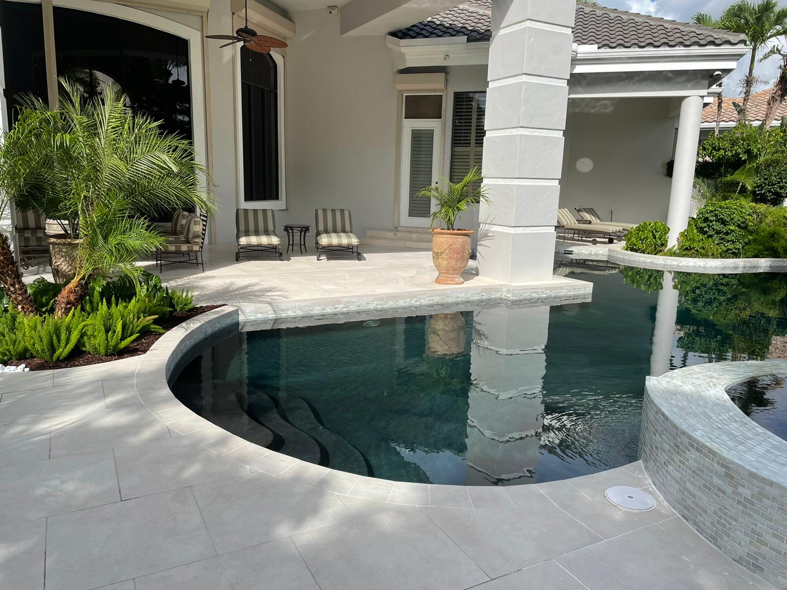 Luxurious backyard pooling area with palm plants, lounge chairs, and elegant pillars, surrounded by tropical greenery and modern architecture.