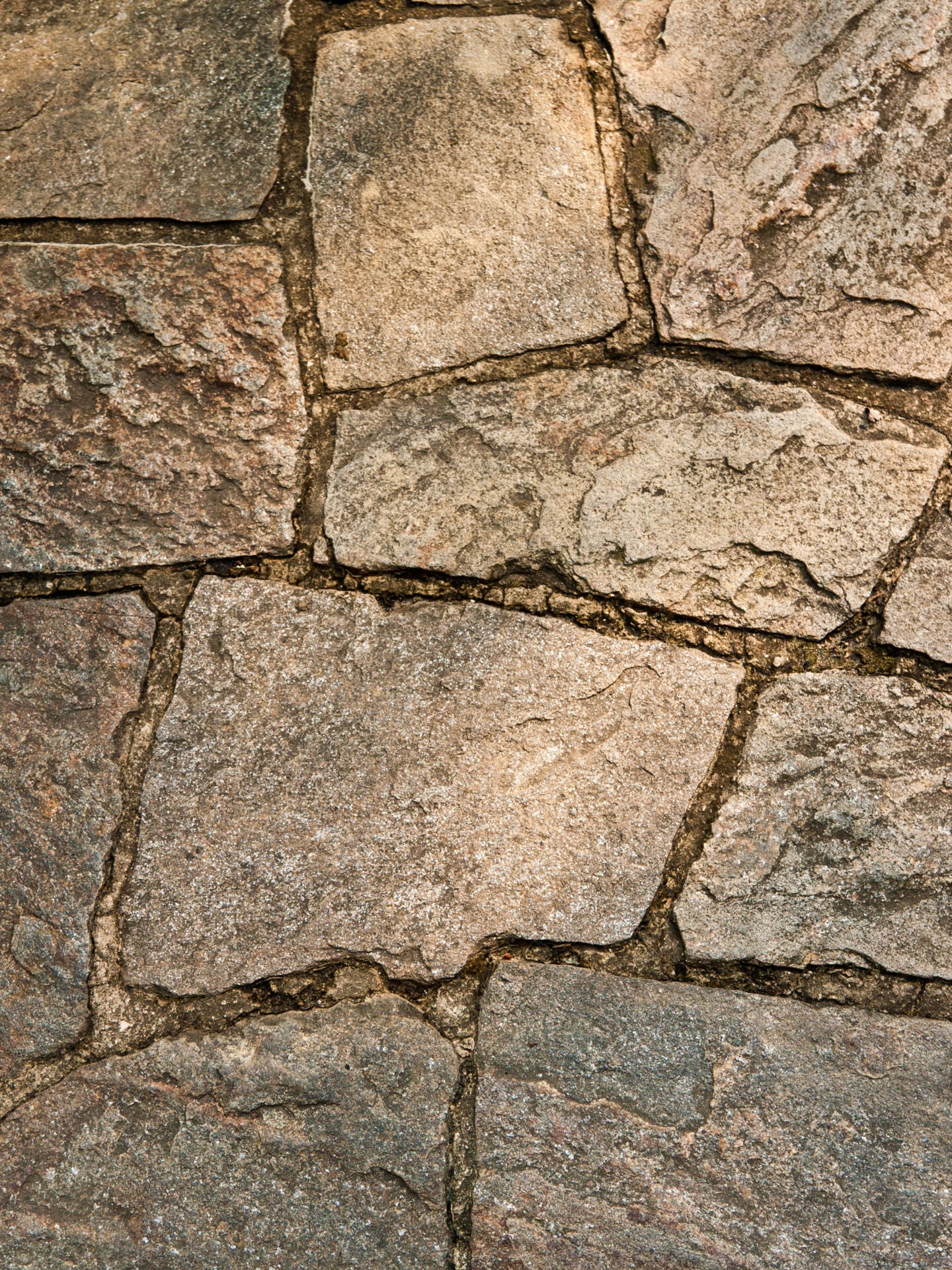 Close-up of a textured, irregular stone pavement, showcasing natural colors and patterns, with visible cracks between the stones. No landmarks or buildings present.