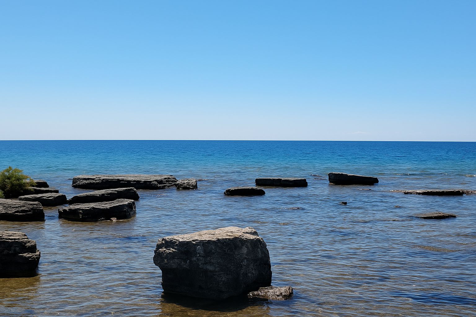 Clear blue sky over a calm sea with large rocks. Peaceful and serene natural setting, no landmarks or buildings visible.