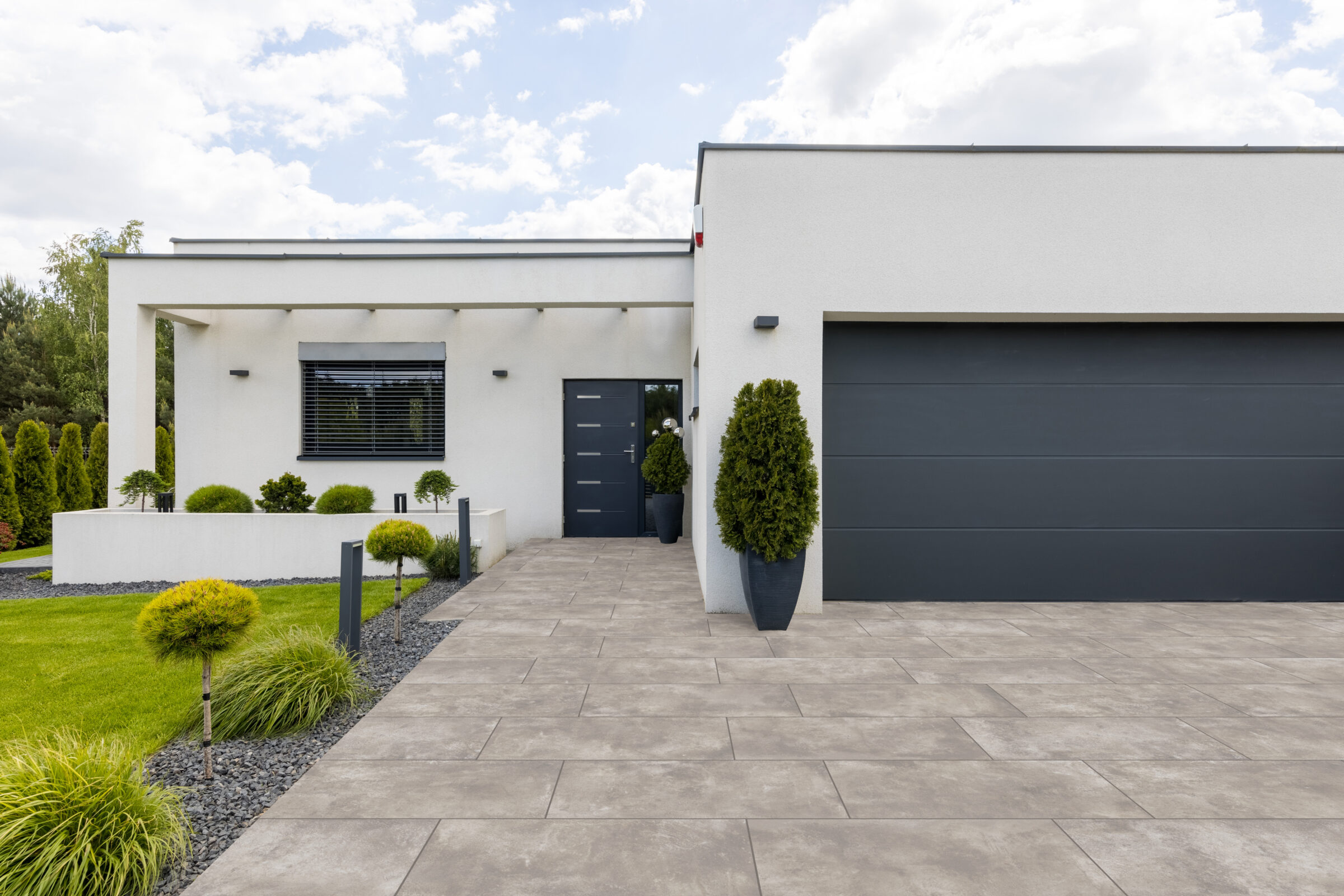 Modern house exterior with clean lines, white facade, dark door, large garage, and manicured lawn. Minimalist design emphasizes simplicity and elegance.