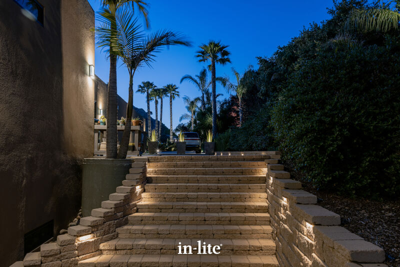 Stone steps with embedded lights lead to a garden with palm trees, under a clear evening sky. Belgian blocks line the sides.