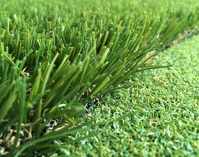 Close-up of green artificial grass blades on a field with a textured surface, blending naturally in a vibrant, lush environment.