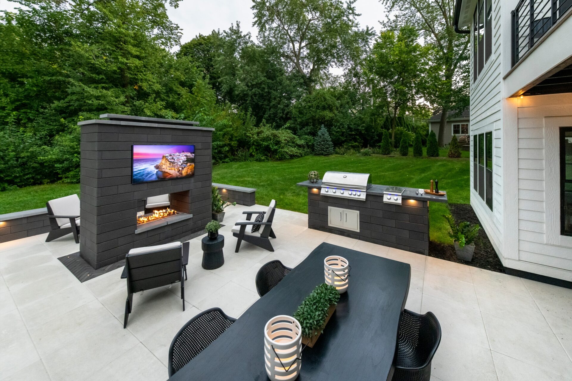 Backyard entertaining area with outdoor fireplace, grill station, television, and dining table.