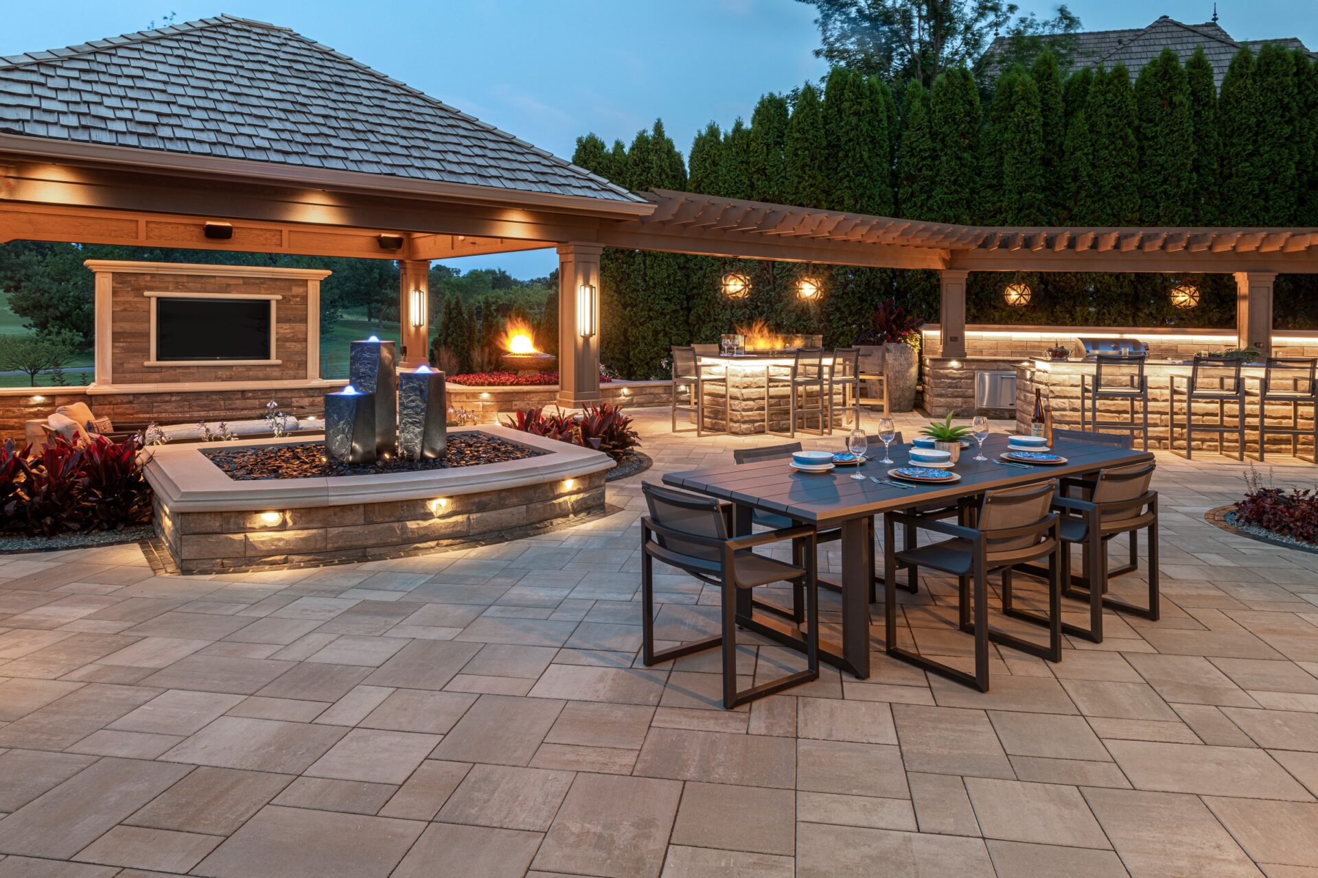 Outdoor dining space at night with fire feature and landscape lighting.