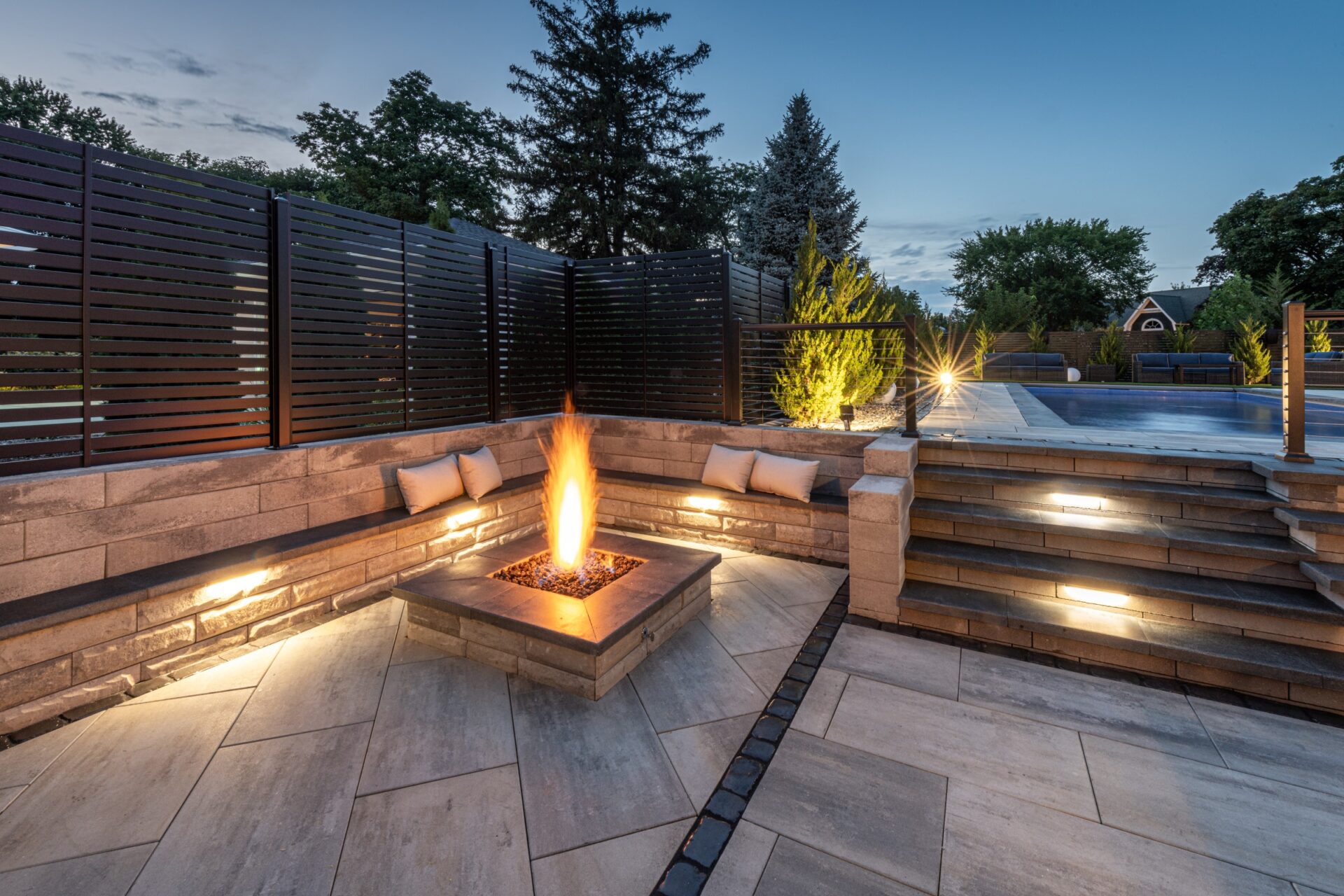 Contemporary outdoor seating area with built-in fire feature and pool lighting at dusk.