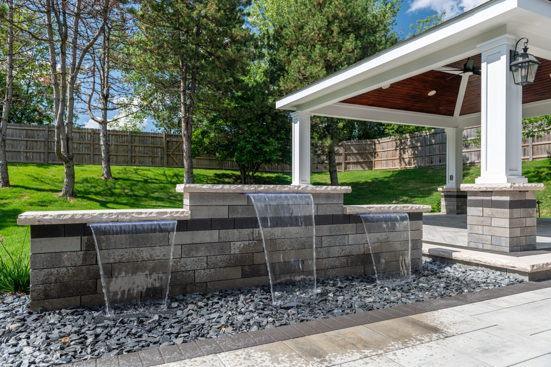 Modern backyard water wall feature with cascading streams beside stone patio.