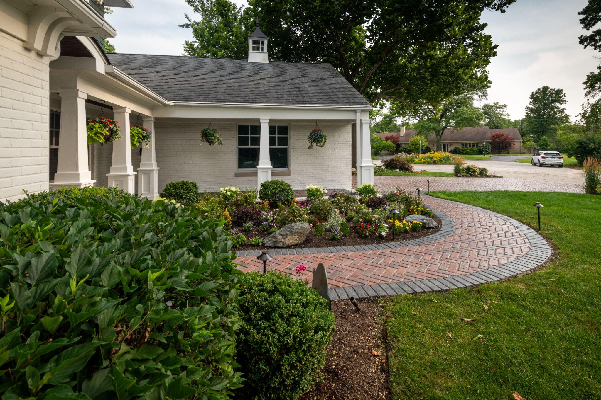 Curved brick walkway with garden bed and landscape lighting