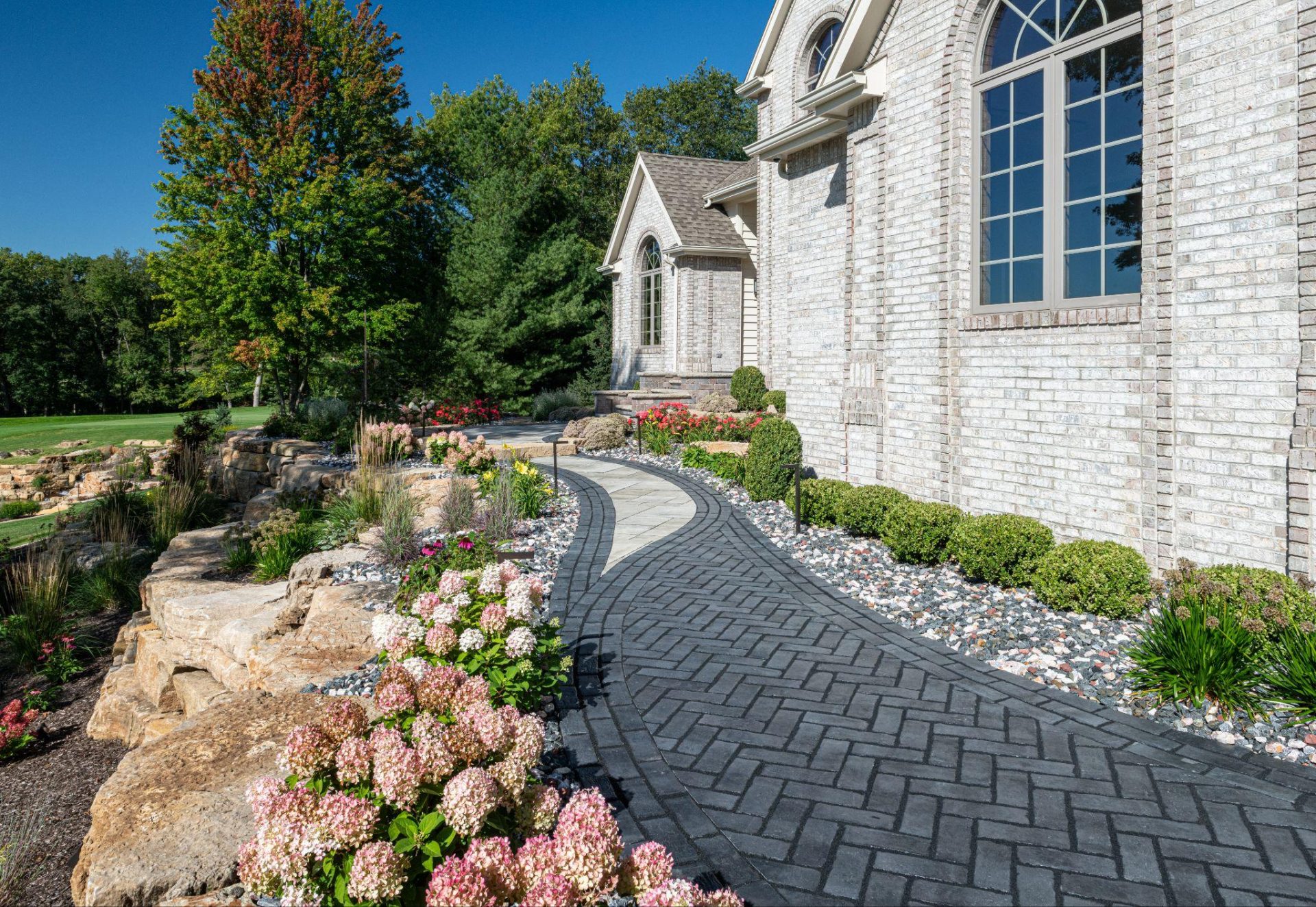 Curved paver driveway bordered with decorative gravel and natural stone