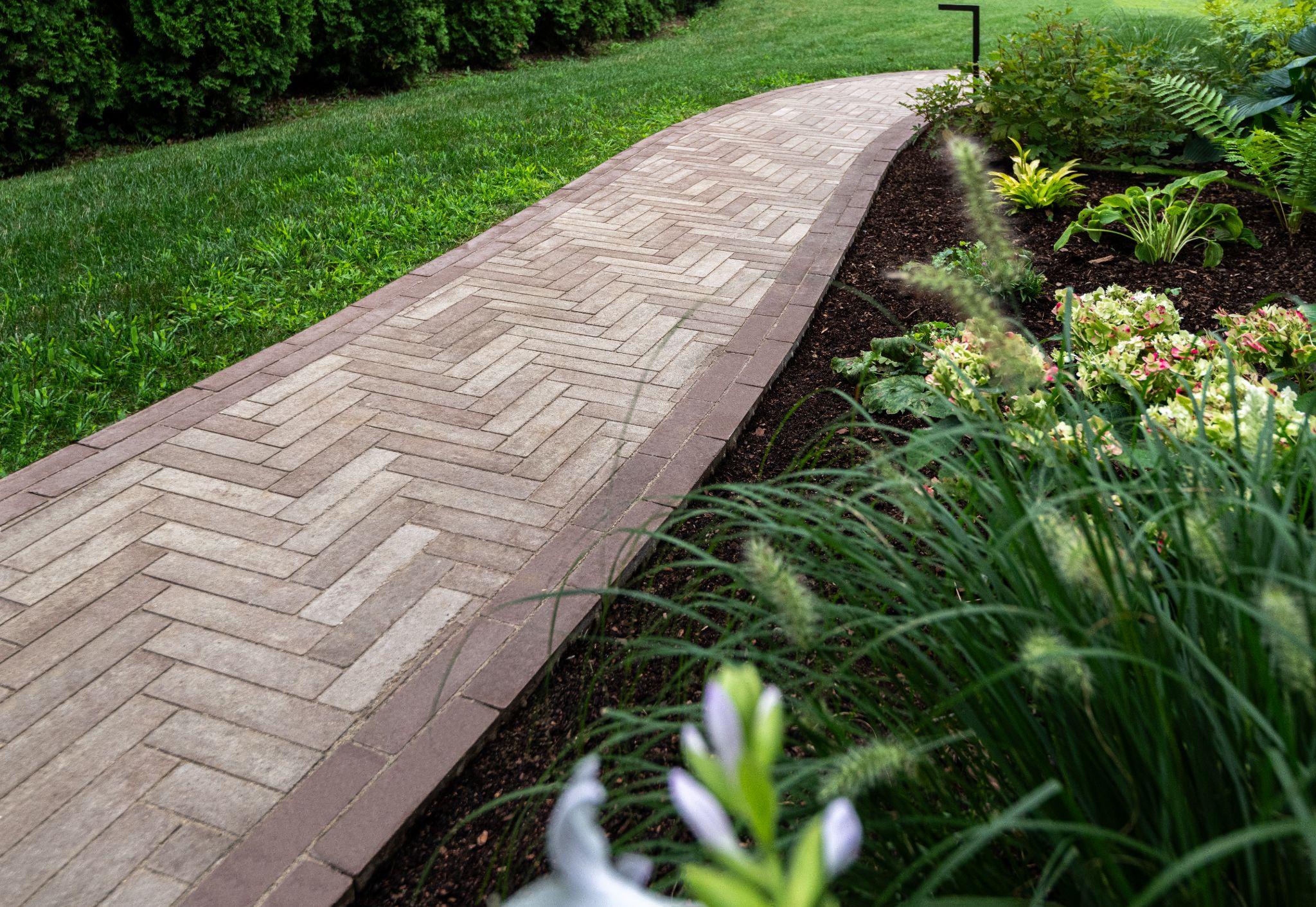Herringbone paver path bordered by lush planting beds