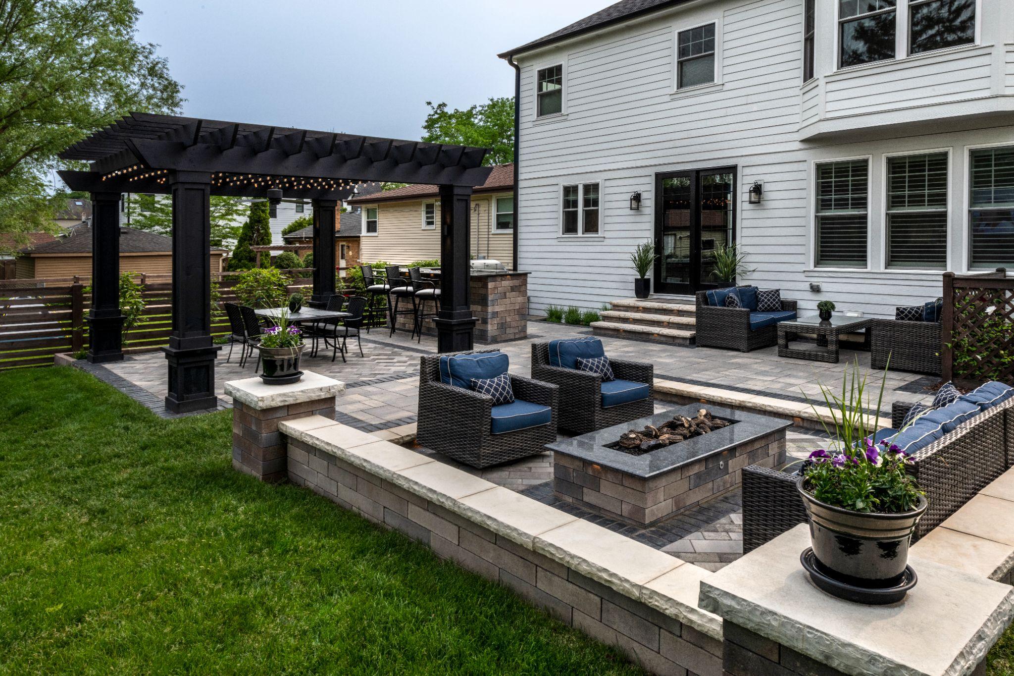 Modern backyard patio with pergola, paver seating area, and built-in fire pit