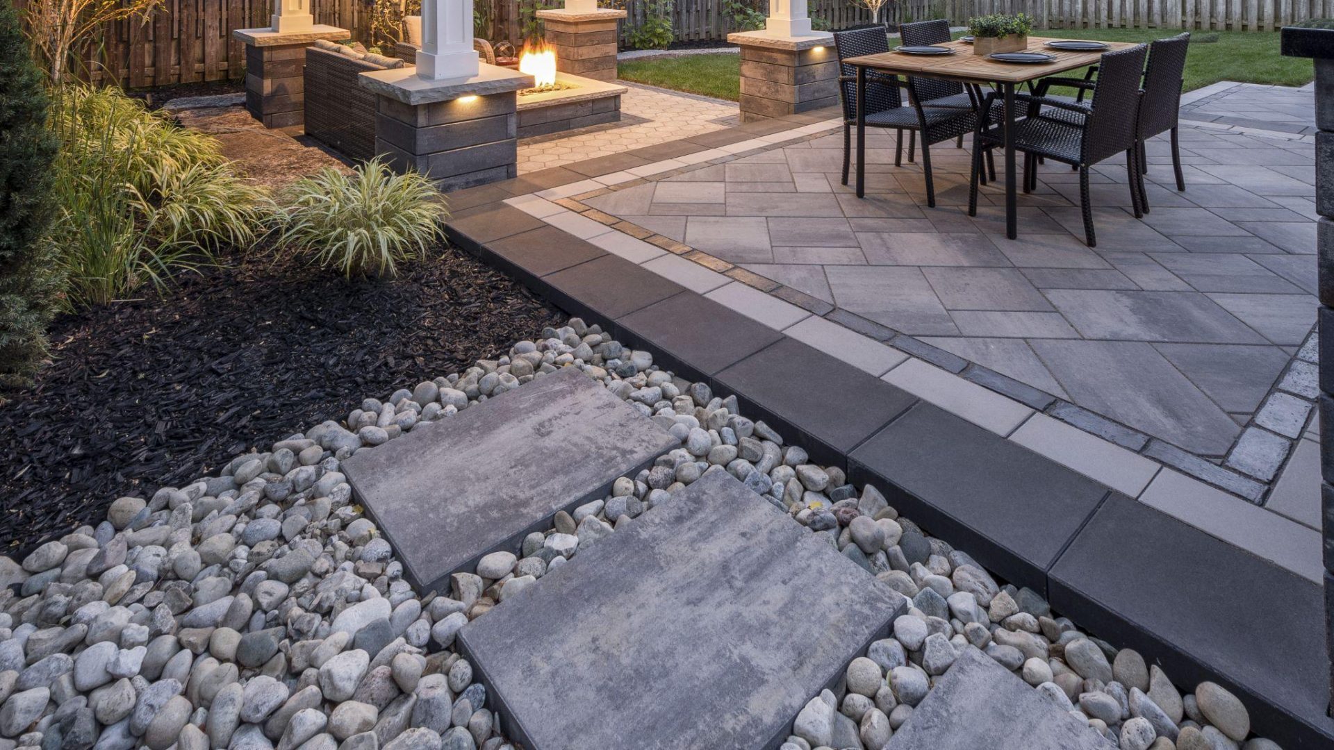 River rock landscaping with stepping stones beside a modern patio and garden bed